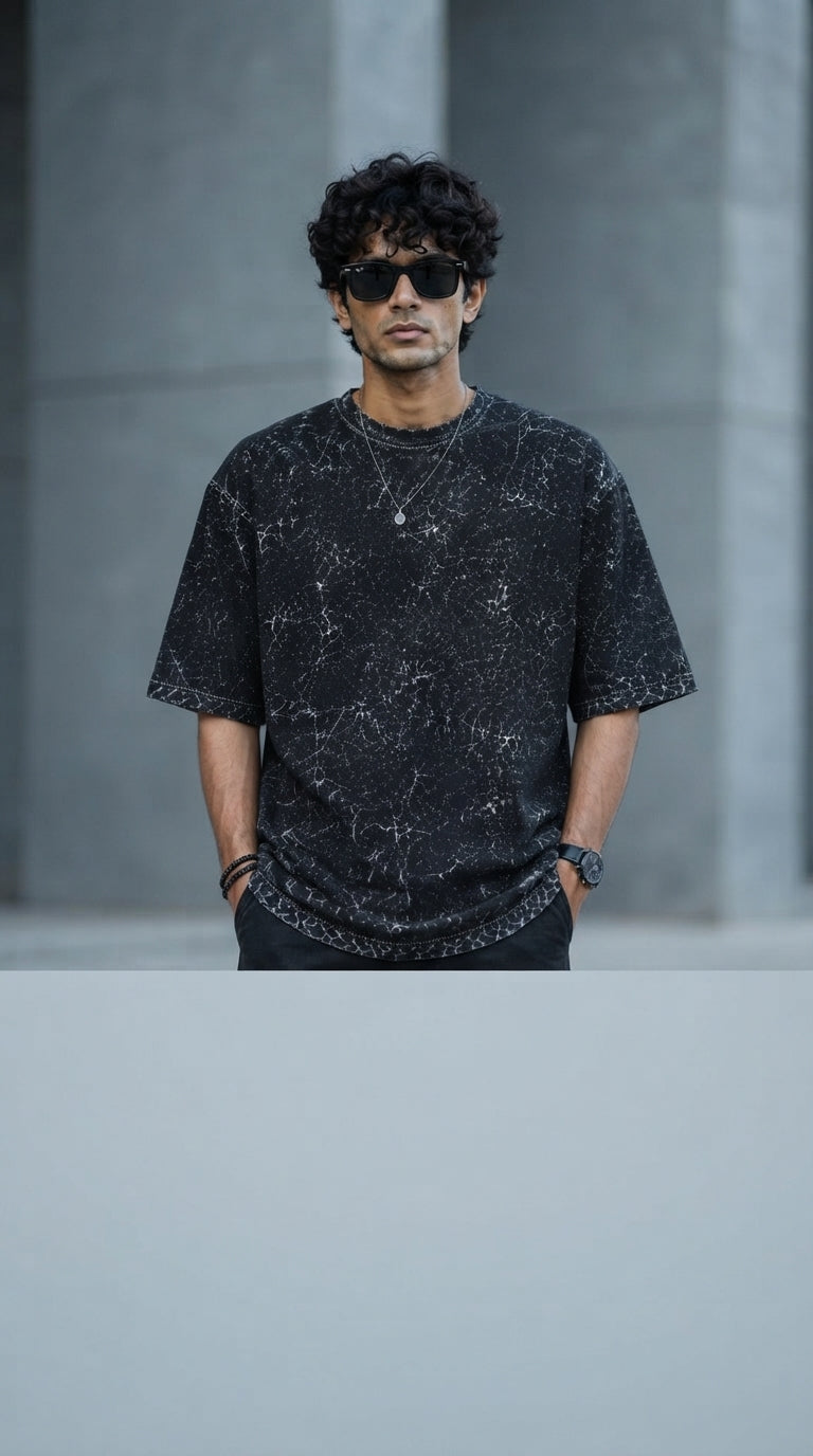 South Asian model wearing a charcoal acid-washed oversized cotton t-shirt against a clean, minimalist gray background.